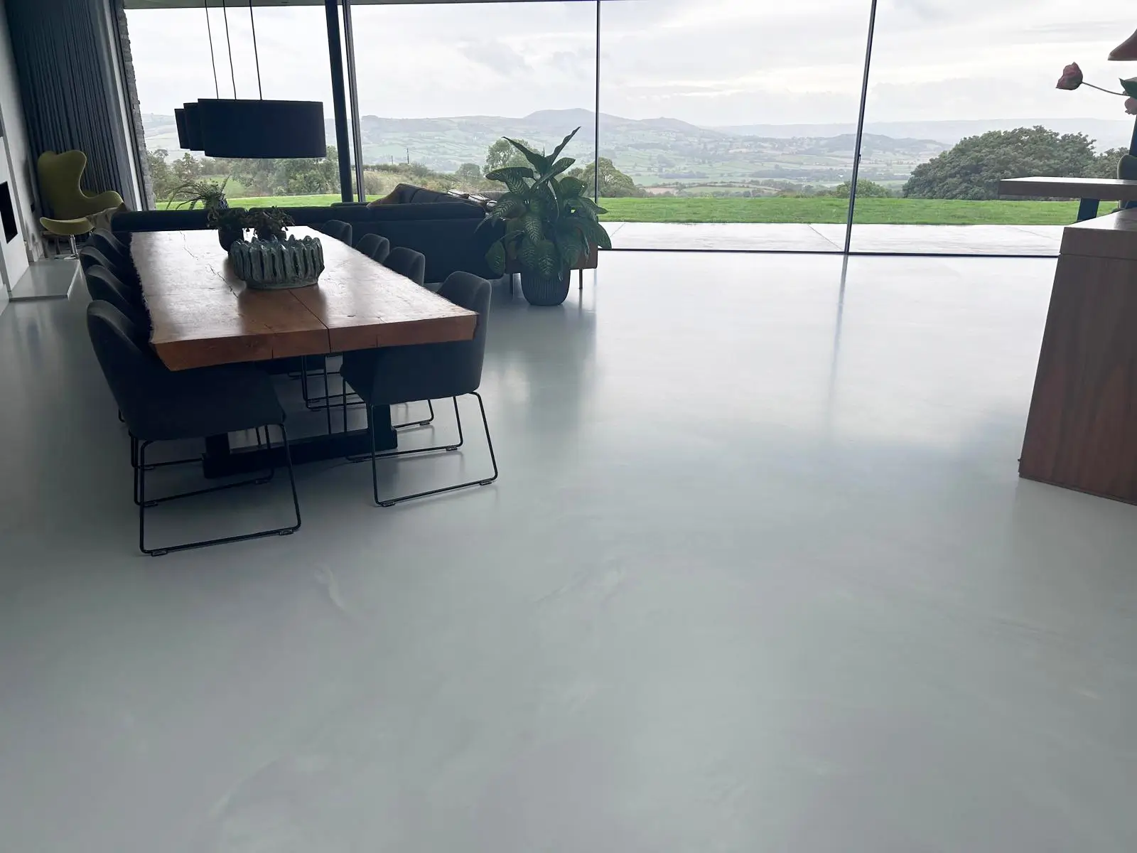 Light grey seamless floor in an open-plan dining and living space with full-height glazing