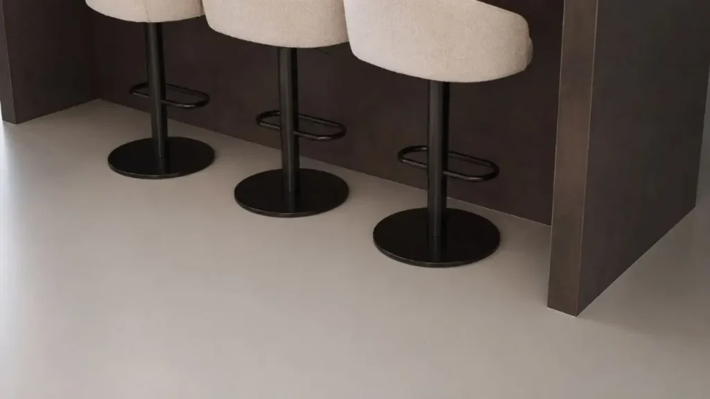 Light grey seamless floor beneath three upholstered pedestal stools at a dark breakfast bar.